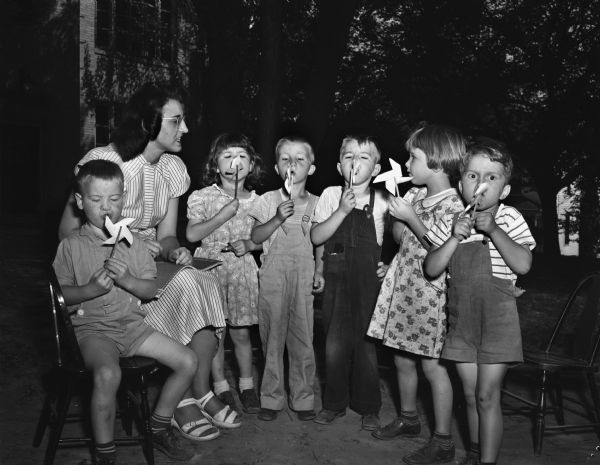 Six children blowing on pinwheels for breath control in front of their teacher, Mrs. Elizabeth Musick, at the summer speech clinic at the Orthopedic Hospital, 1415 Linden Drive. The clinic is one of three clinics for handicapped children run by the University of Wisconsin.