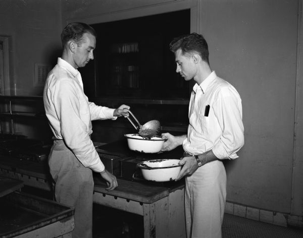 Two university students helping serve dinner to patients at Mendota State Hospital. They are John LeSeur from Cornell University on the left, and Roy Kletti from the University of Wisconsin on the right. (Mendota Mental Health Institute).