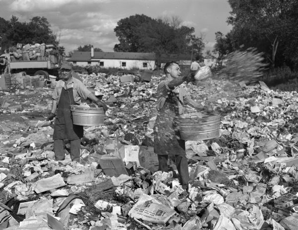 Two men are scattering barium carbonate rat poison in a city dump located at the end of Fern Drive off Highbury Road near University Avenue. The land was owned by Dudley Davis. A dump caretaker lived in a small trailer at the rear of the dump.