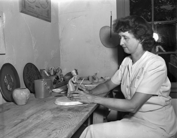 Mrs. Joseph W. (Frances) Vilas, Maple Bluff, is shown working on a figurine, with a background of other pottery pieces she has made.