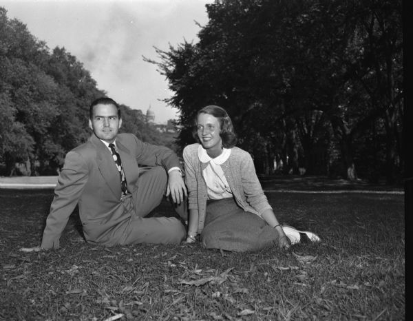 Charles Johnson and Margaret Haas, two students in charge of University of Wisconsin orientation week activities, sitting on the grass on Bascom Hill. The Wisconsin State Capitol is in the far background.