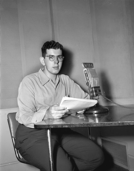 Unidentified young man (Landsman?) seated at a table with a WIBA microphone.