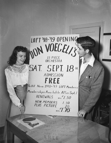 A young woman and a young man with a poster announcing the '48-'49 opening of the LOFT on September 18, with Don Voegeli's 15 piece orchestra.