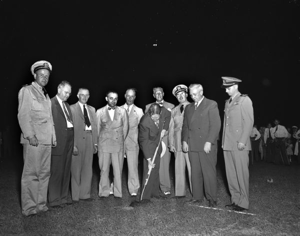 City manager Leonard G. Howell, breaking the ground with a shovel, at the ground-breaking ceremony for the new Naval Reserve training center in Kendall Field, 1046 East Washington Avenue. Looking on are, left to right: Lieut[enant] John G. Jamieson, public information officer of the reserve unit; F. Halsey Kraege, president of the Madison and Wisconsin Foundation; R.L. Ethun, president of the East Side Business Men's Association; J.W. Jackson, executive director of the Madison and Wisconsin Foundation; James R. Law, Chairman of the reserve civilian advisory council; Lieut[enant] Com[man]d[e]r R.J. McCue, assistant inspector-instructor of the reserve in Madison; Governor Oscar Rennebohm; and Lieut[enant] Com[man]d[e]r G.L. Block, inspector-instructor of the reserve in Madison and La Crosse.
