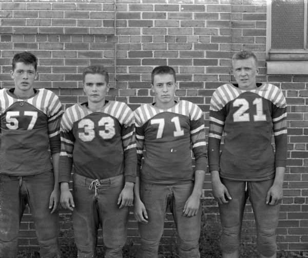 Portrait of four West High School football players in uniform.