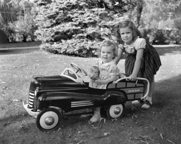 Two young girls outside with a toy pedal station wagon. Possibly children of a Harley family.