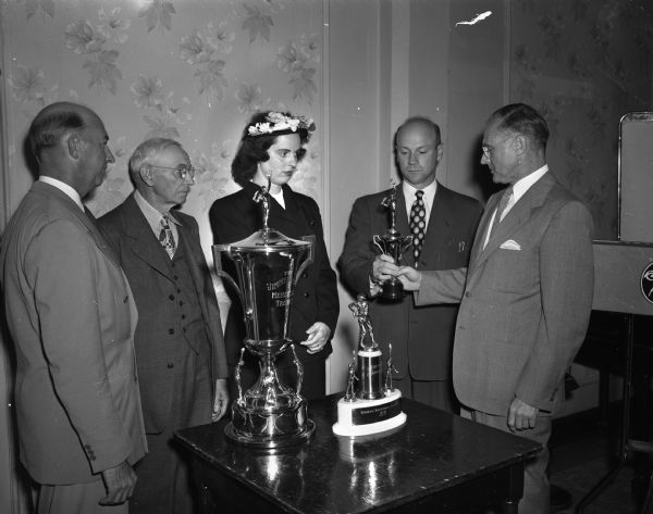 John Gerlach, second from the right, was named "Most Valuable Player" in the Industrial League for 1948 and is the first to receive the Jimmy Dodge Memorial Baseball Trophy. Dr. Ray Huegel, right, is presenting Gerlach with a miniature replica of the Dodge Trophyh. Gerlach also won the League individual hitting trophy which is on the table in the foreground. The others attending, are, left to right: Cy Dodge, West Bend, a brother of Jimmy Dodge; Nels Dodge, Spring Green, Jimmy's father; Mrs. Fritz Berndt, Prairie du Sac, daughter of Jimmy Dodge.