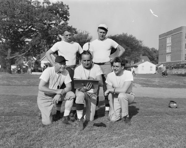 New head football coach for Madison East High School, Herbert "Butch" Mueller, is kneeling in the center with his other coaches. Ferris "Red" McKinley is kneeling at the left and Elmer Homburg kneeling at the right. In back are Milt Diehl, left, and Larry Johnson.