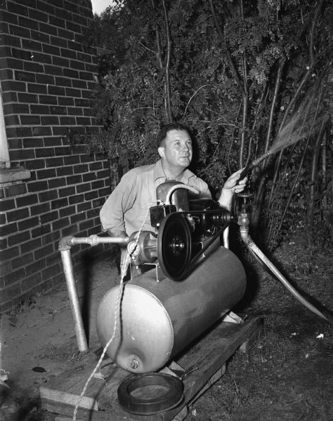 Harry Hall, 1848 Yahara Place, is shown watering his lawn with a hose attached to a electric air compressor which is pumping water from an eight foot pipe Mr. Hall drove into the ground.