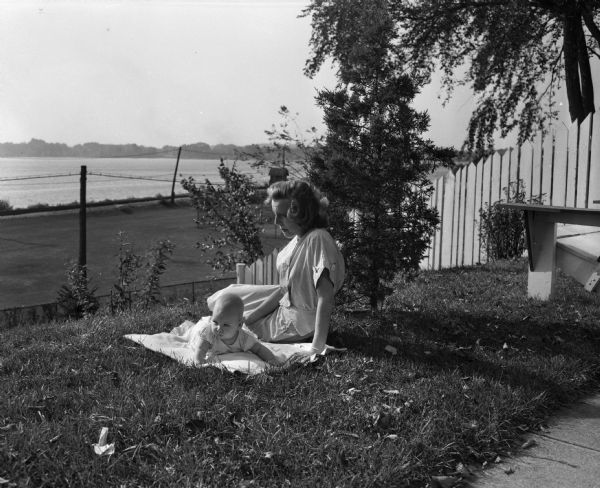 Mrs. Theodore Statz and her 6-month old daughter Cindy in the yard of their basement apartment at 425 West Wilson Street. They are soon to be evicted because their apartment does not meet building code limitations. Lake Monona is in the background.