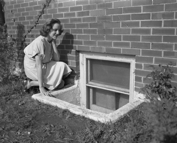Mrs. Theodore Statz outside a window of her family's basement apartment at 425 West Wilson Street. They are soon to be evicted because their apartment does not meet building code limitations.