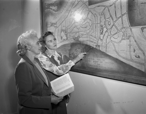 Mrs. George (Frances) Burrell, 1509 Wood Lane, at left, and Mrs. Charles L. (Myrtle) Fluke, 3003 Harvard Drive, at right, inspecting a map of the village of Shorewood Hills which hangs in the village hall. Mrs. Fluke is chairperson of the directory committee of which Mrs. Burrell is one of her fellow members.