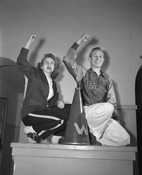 Cheerleaders Mary Lita Jensen, West High School, and Bob Stone, East High School, demonstrate cheers to keep up the morale of their respective football teams.