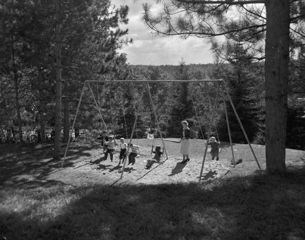Five children with one adult are shown playing on swings at Eagle Heights, a University of Wisconsin-Madison housing development built for faculty families.