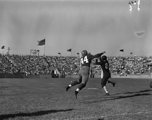 University of Wisconsin vs. University of Indiana football game at Camp Randall Stadium. Bobby Petruska, #44, intended pass receiver for Wisconsin, is shown leaping for the ball which is intercepted by Ernie Kovatch, #81, of Indiana. In the background fans are in the stands.