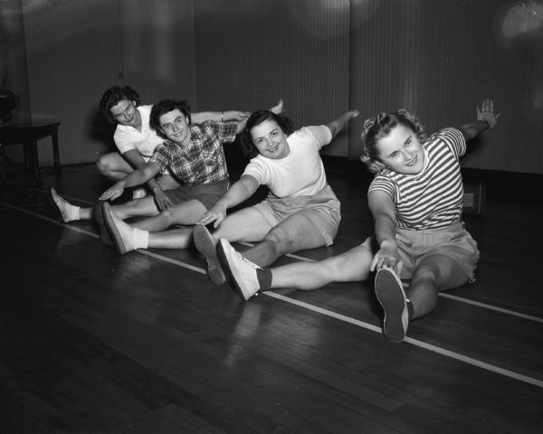 Three members of the YWCA doing floor stretching exercises under direction of, extreme left, Mrs. Robert L. Nelson, 75 Randall Park, YWCA physical education instructor. Stretching are, left to right: Bernice Williams, 1904 Kendall Avenue; Mrs. George (Edna) Craig, 305 Norris Court; and Mrs. K.D. Jones,(Eleanore) 121 Hamilton Avenue.
