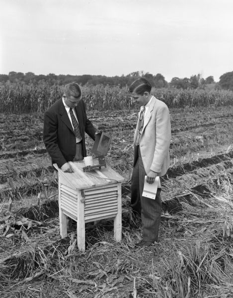 Assistant Professor Reid Bryson of the University of Wisconsin Meteorology department, and student Charles Thorngate, Middleton, examine an instrument located in a cornfield on campus near the Willows that measures soil temperature.