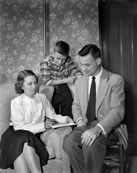 Ronnie Hinrichs is shown looking on as his mother, Mrs. Arthur S. Hinrichs, prepares to sign a contract giving Ronnie permission to become a WSJ carrier boy. Don Neu, district carrier boy manager, sits to the right of Mrs. Hinrichs.