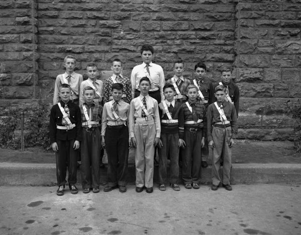 Group portrait outdoors of the members of the Father Petti School (St. Raphael congregation) safety patrol crossing guards: Left to right: first row: Dick Barry, Stanley Triggs, John Emmerich, Joseph Uselton, John Rhatigan, Stephen Triggs, and Willard Spragues. Second row: Bob Rubak, Edward Page, Bill Coster, Richard Elsner, Richard Riley, Bob Grady, and Carl Barry.