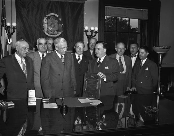 Thomas N. Boate, public safety director of the Association of Casualty and Surety Companies, presents an award to Wisconsin for its high place in the training of young drivers. Present at the award presentation are, from left, Voyta Wrabetz, industrial commission chairman; Ben L. Marcus, director of the motor vehicle department; Henry H. Bush, Madison insurance man; Governor Oscar Rennebohm; Attorney General Grover Broadfoot; Lorentz H. Adolfson, director of the University of Wisconsin extension division; Mr. Boate; Mike Mack, vice-chairman of the State Highway Commission; C.L. Greiber, director of the state vocational and adult education; and John L. Sonderegger, insurance commissioner.