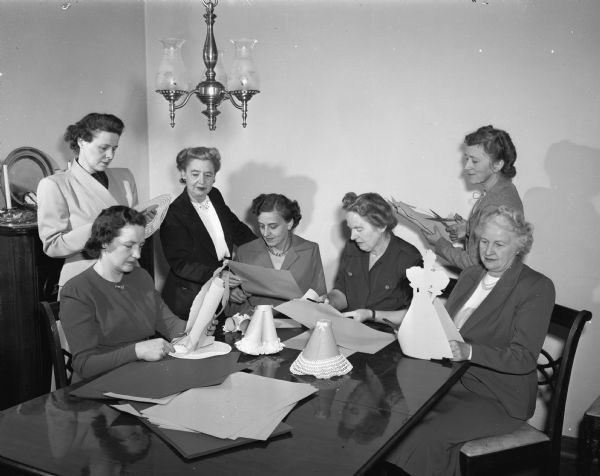 The University League committee members, wives of University of Wisconsin faculty, make table decorations for the Centennial luncheon at the Memorial Union. Seated, left to right: Mrs. Henry L. (Harriet) Ahlgren, Mrs. Ludvig C. (Harriet) Larson, Mrs. William P. (Luella) Mortenson, and Mrs. Robert Nohr Jr., president of the League. Standing left to right: Mrs. I.H. Adolfson, Mrs. T.R. (Lena) Truax, and Mrs. Richard (Lois) Hartshorne.