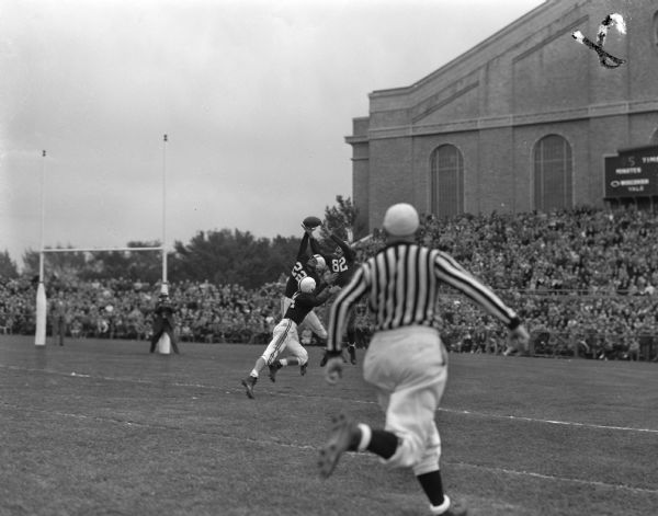 Wisconsin football player, end Ken Sachtjen (82), tries to grab a pass from Wisconsin player Forrest "Frosty" Parish while Yale player Robert "Tex" Furse (22), leans up to snatch the ball. Yale tackle Brooks Naffaiger (44), is ready to tackle Sachtjen if the pass is completed.