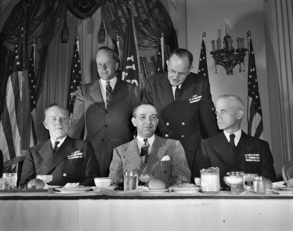 Group portrait of men at the speaker's table for the banquet that climaxed Navy Day observance. Seated left to right are: Rear Admiral E.W. Hanson, commandant of the 15th naval district, Panama, guest speaker; Maurice Pasch, president of the Madison Navy league; and Capt. J.F. Hurff, professor of naval science at the University of Wisconsin.  Standing left to right are John Jamieson, naval public information officer for the Madison area; and Rear Admiral R.T. Coudrey, former Oregon resident, who served as fleet maintenance officer on Admiral Halsey's staff during World War II.