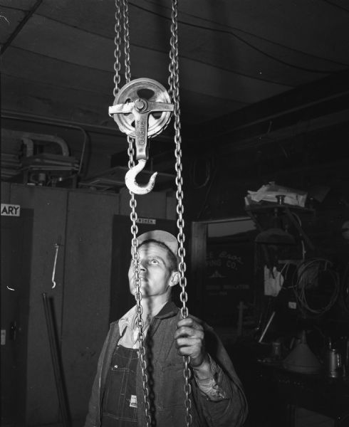 John Ochalle, employee of the Durfee Brothers Roofing Company, who discovered evidence of a burglary at the company's place of business at 1804 South Park Street. Ochalle is shown with the chain hoist that the burglars used to remove a 500 pound safe from the roofing firm office.