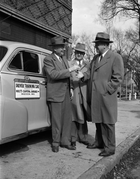 Ralph Hult, president of Hult's Capital Garage, presenting the keys to a dual control driver training car to Richard Bardwell, director of the Madison vocational school (right). Looking on in the center is Dean Fay Elwell of the University of Wisconsin commerce school and chairman of the AAA advisory committee in Madison. The car was loaned to the school for use in its adult driver training course through arrangements made by the American Automobile Association and Hult's garage.
