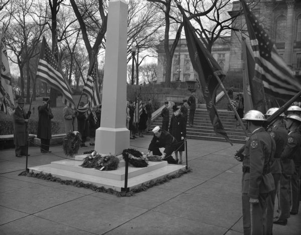 Color bearers from the National Guard, the Veterans of Foreign Wars, the two American Legion posts, the Spanish-American War veterans, their auxiliaries, and wreath bearers march past the memorial obelisk on the lawn of the Wisconsin State Capitol during Armistice Day commemoration ceremonies.