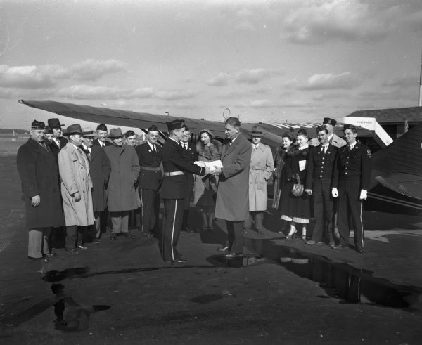 American Legion members in front of a plane at the Madison airport. Membership Chairman R.C. Golden is handing 1949 membership cards to the pilot Colonel Lester Maitland. The cards will be taken to Milwaukee as part of the annual aerial membership roundup.