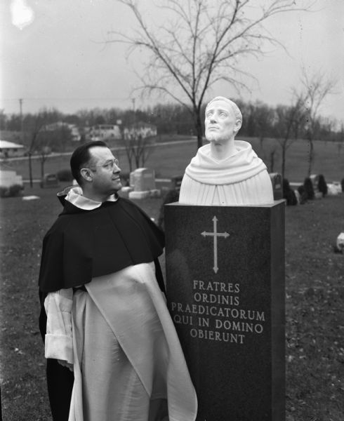 Rev. J.B. Schneider, O.P., pastor of Blessed Sacrament Catholic Church, looking at a newly installed bust of St. Dominic de Guzman, Spanish priest who founded the Catholic Order of Preachers at Toulouse, France in 1215. The white marble bust is installed on top of the black granite shaft marking the Dominican priests' plot at Calvary Cemetery.