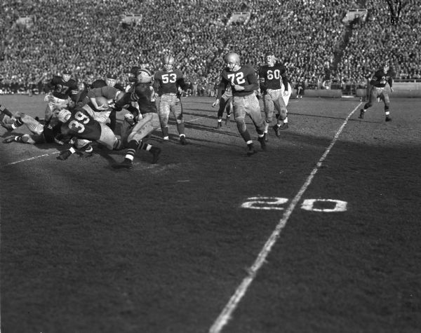 University of Wisconsin football player Gene Evans, in the center, carries the football for a six-yard run on the team's drive to their second touchdown. Also in the picture are Wisconsin player  Robert "Red" Wilson (53,) and University of Marquette players Sherwood Soip (39,) and Phil Daly (37.) Wisconsin won the game 26 to 0.