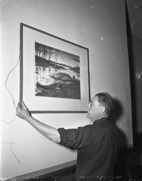 Byron C. Jorns hanging a watercolor painting for an exhibit at the Madison Bank and Trust Company. A series of exhibitions was arranged by the bank to encourage Madison area artists, and to familiarize the public with their work.
