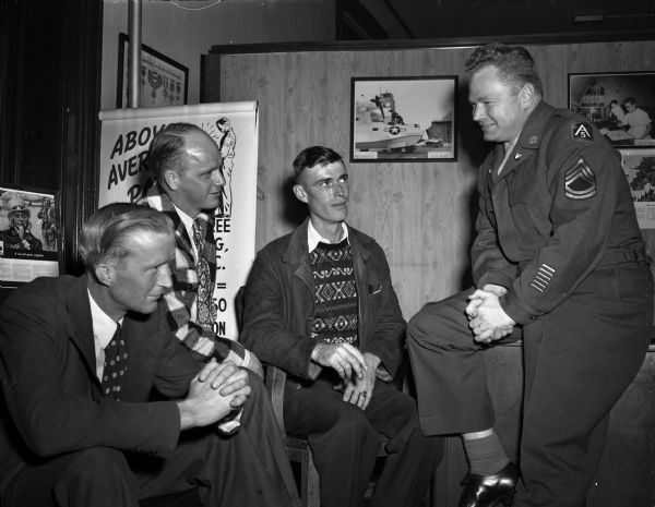 Sgt. Tom Sorenson, processing sergeant for Madison area U.S. army draftees, briefing the first recruits to be processed through the Madison army recruiting station under new draft regulations.  Left to right: Delbert Popp, Belmont; Delbert Ramsden, Route 1 Avoca; Robert J. Harker, Route 4, Mineral Point; and Sgt. Sorensen.