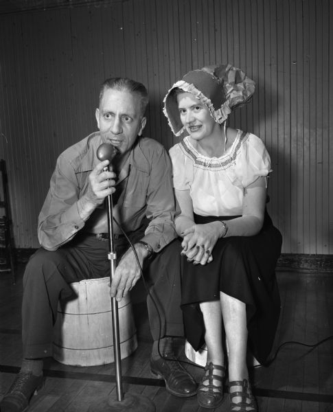 Members of the Madison Who's New Club at a barn dance at the YWCA gymnasium. Square dance caller, Frederic E Risser, and his wife Elizabeth wearing a bonnet, are sitting on barrels.
