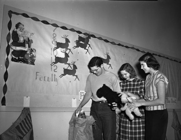 Fritz Hanson, Peggy Huiskamp, and Winifred Grant of Wisconsin High School, are shown checking on the drive for toys which the school's Junior Red Cross Council is conducting for the children's home at Sparta.