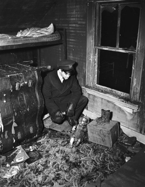 Police Officer Robert O'Neil looking at charred doll and little red boots found in the debris in the room in a tenement-type house, 15 South Bedford Street, where a fire killed Florence Dinger and three of her children.