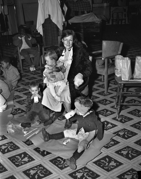 Valera Widener and her children: Norma (on her lap), Franklin (left), and Lyall (right), in Baron Brothers Department Store drinking milk provided by the Empty Stocking Club. The family lost their housing due to the fire in the tenement-type house at 15 South Bedford Street, where a fire killed Florence Dinger and three of her children.