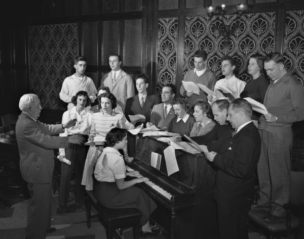 Fifteen University of Wisconsin students in the Community Leadership in Recreation curriculum are shown singing under the leadership of Emeritus Prof. E.B. Gordon. Jeanette Thorson is playing the piano.