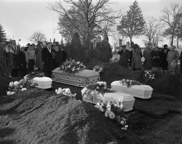 The funeral for the fire victims of the Bedford Street fire was finalized in the Middleton Junction Cemetery. The caskets are shown as the mourners await the final words of the committal by the Reverend Charles Puls. The victims of the fire are Florence Doreen Dinger, the mother, and her children, William Fred Dinger Junior, Shirley Jane Dinger, and Judeen Louise Wipperfurth.