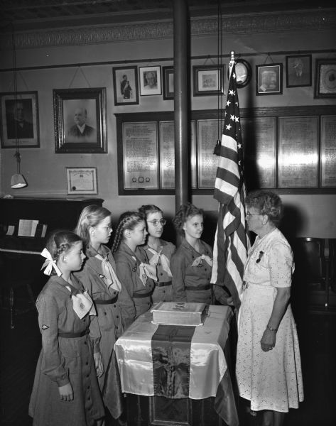 "Mrs. Louise Watson, patriotic instructor of the Lucius Fairchild Women's Relief Corps, is shown as she presented an American flag to Girl Scout Troop 115 of the Lowell school in a ceremony at the GAR hall." The Scouts in the picture (from left to right) are Carl Kruse, Janet Schuldt, Elizabeth Straus, Joan Denhof, and Mary Ann Serstad.