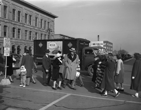 Street scene at East Washington Avenue and Pinckney streets with pedestrians crossing the street. Advertisement on the side of a parked Railroad Express Agency Truck has Santa Claus saying "And to all, milk and good health."