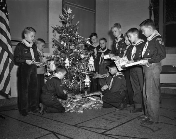 Ten cub scouts from Cub Pack 319 placing gifts for less fortunate boys and girls under a Christmas tree at Marquette School. Standing, left to right, are Jimmy Bond, Martin Clark, Billy Schueman, Jackie Schroeder, Wally Masset, Loyde Childs, Teddy Burr, and Billy Ward. Kneeling are Robin Barkenhagen and Robert Simon.