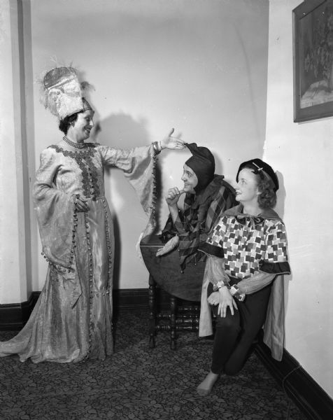 Two alumnae members of the Madison chapter of Phi Beta, speech and music sorority, rehearsing for their part in the "Old English Revels" for members and their husbands. Left to right are: Mrs. Stuart (Carol) Reid (?) as the lady of the manor house, Charles C. Thompson, both a tumbler and "half" a dragon, and Mrs. Edward DeGroot as a page.