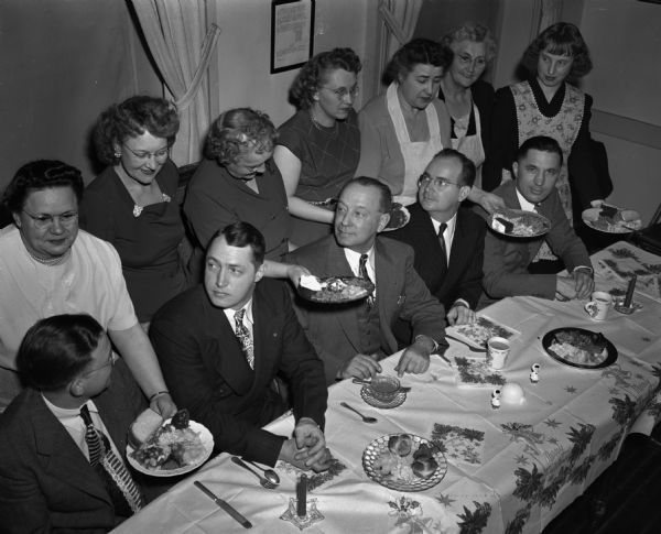 Elevated view of five seated members of the Madison branch of Letter Carriers (#508) being served a pot luck supper in their honor by seven women at the GAR hall.