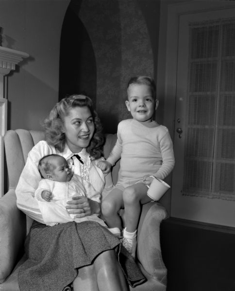 Mrs. William (Bette Gillette) Stilwell and her two children. The infant in her lap, Janet, is 4 months old, and sitting on the arm of the chair is Joey, who is 3 years old.