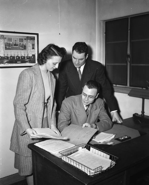 Mrs. Ken H. (Virginia) Taylor, secretary of the Madison Legal Aid Society, arranging a case file for William, Oshkosh, (seated) a University of Wisconsin law student and staff member of the society. Looking on is Jack R. DeWitt, a law school instructor and faculty advisor to the student staff.