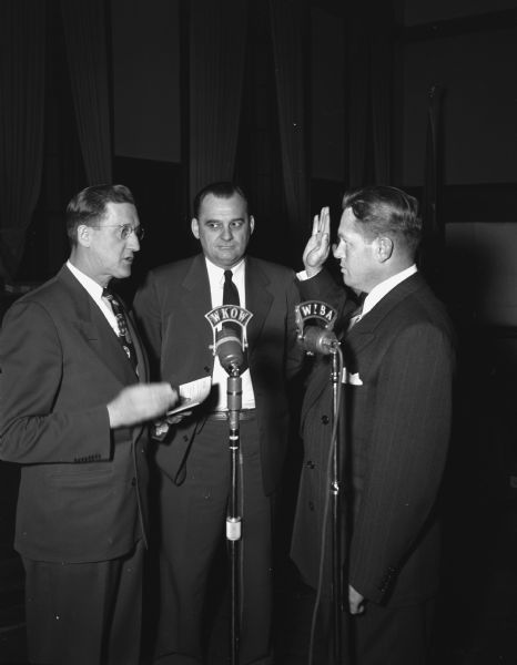 City Clerk Alfred W. Bareis swears in police chief Bruce Weatherly in front of WKOW and WIBA microphones.  George Forster, city finance director and acting city manager is looking on.  Alfred W. Bareis was mayor from 1955-1956.