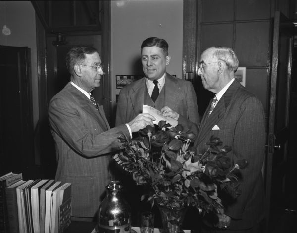 Joseph J. Wirka, former superintendent of mails, on the left, is shown receiving the keys to the post office from Walter J. Hyland, on the right, retiring postmaster with 15 years of service, after being sworn in as Madison's acting postmaster by Merton G. Eberlein, center, Madison district post office inspector. The roses in the foreground were presented to Hyland by the clerks and supervisors.